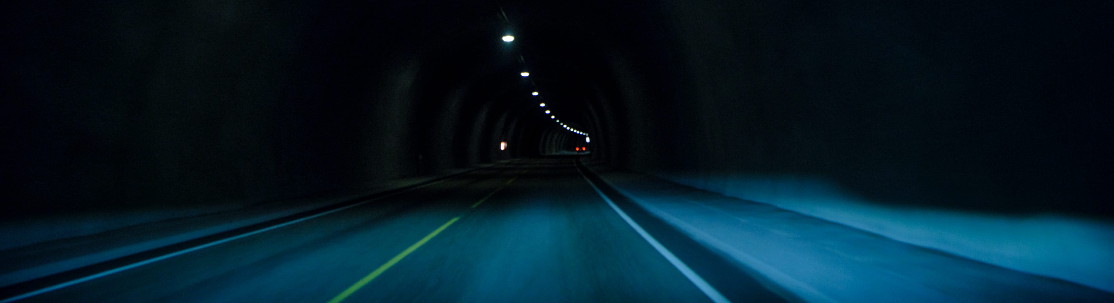 The view from inside a tunnel, capturing a long and narrow passage illuminated by spaced-out overhead lights