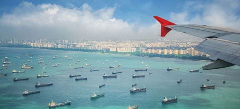 Avión de carga volando sobre el mar repleto de buques llegando a puerto.