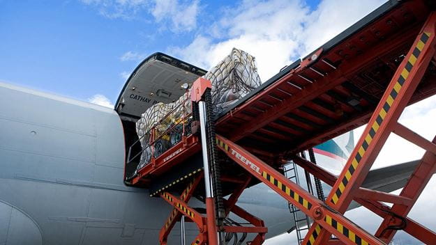 A cargo plane with its open cargo hold being loaded with boxes and pallets of cargo using a red loading ramp.