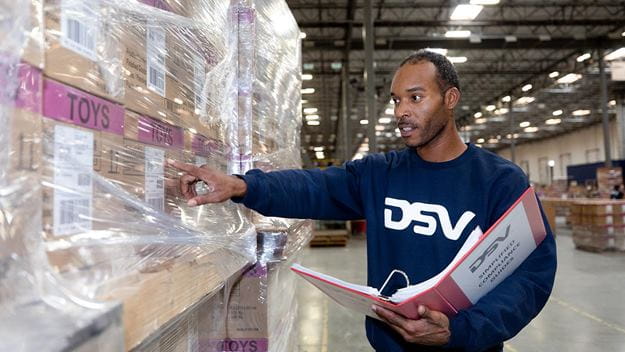 A DSV employee is handling record administration in a DSV warehouse with large racks of toys.