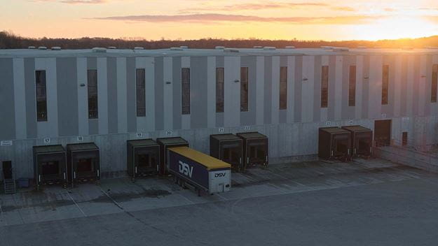 Un remolque de DSV estacionado en un muelle de carga de un moderno centro logístico al atardecer.