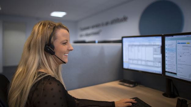 Nainen istuu työpöydän ääressä, puhuu asiakkaan kanssa ja samalla kirjaa ongelman koneelle.