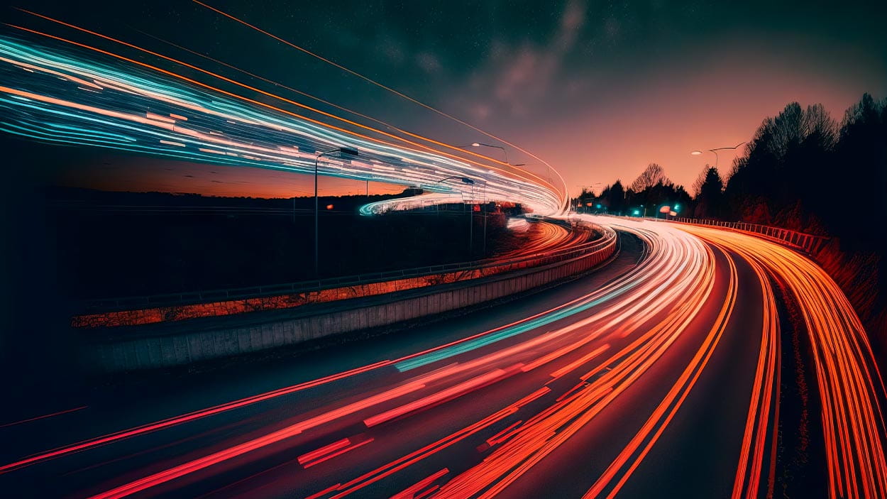 a long exposure photo of a highway at night with lights on it and trees in the background with a sky filled with clouds.