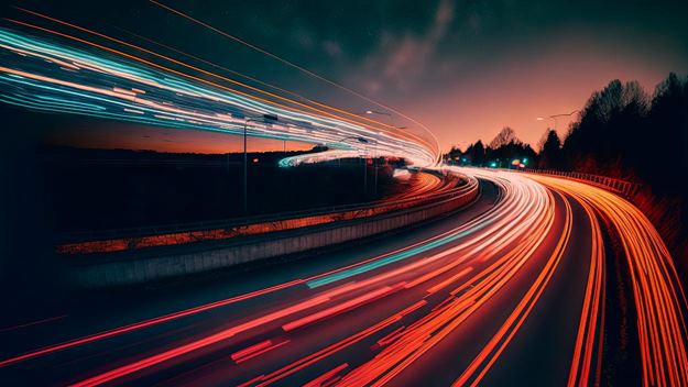 a long exposure photo of a highway at night with lights on it and trees in the background with a sky filled with clouds.