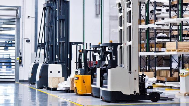 A row of reach trucks parked in a warehouse aisle, with tall shelving in the background.