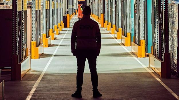 A DSV staff standing in a warehouse aisle, surrounded by shelves filled with various products.