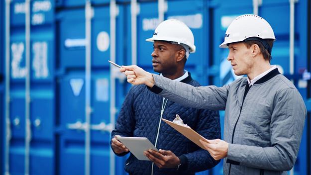   two men with hardhats inspecting containers at a dockyard