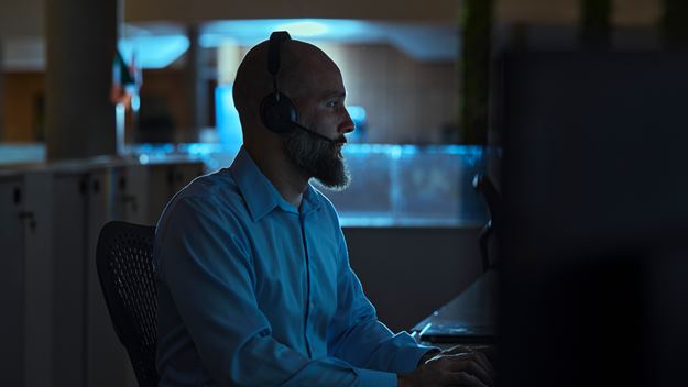 Male office worker with a headset looking at a computer screen