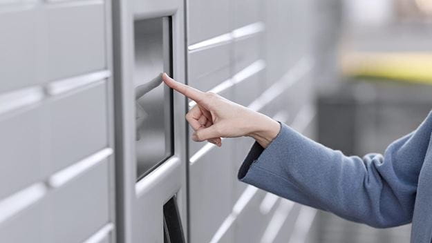 Hand pressing button on a parcel locker to retrieve or send a package.