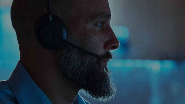 A man wearing a headset working at his desk in an office environment. One image is split into 6 separate images showing a part of the image