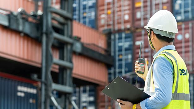 Male DSV employee with white safety helmets and yellow safety west inspecting containers