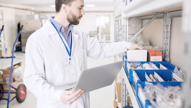 Hombre con bata revisando insumos médicos en almacén