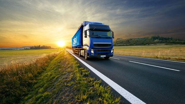 Camión de carga de DSV en movimiento en carretera rodeada de campos durante el atardecer.