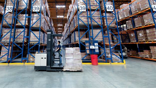 Almacén de DSV donde se observan estantes con cajas de mercancía y una persona en un montacargas en el medio de la fotografía.
