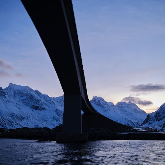 bridge over water near snowy mountains
