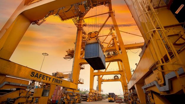Busy container terminal with cranes and cargo handling at sunset.
